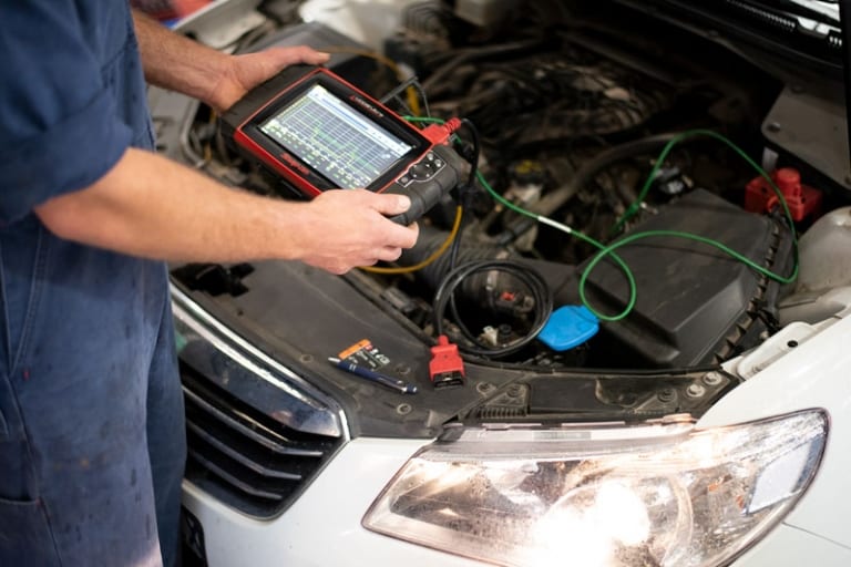 Technician running electrical diagnostics on a car battery and wiring