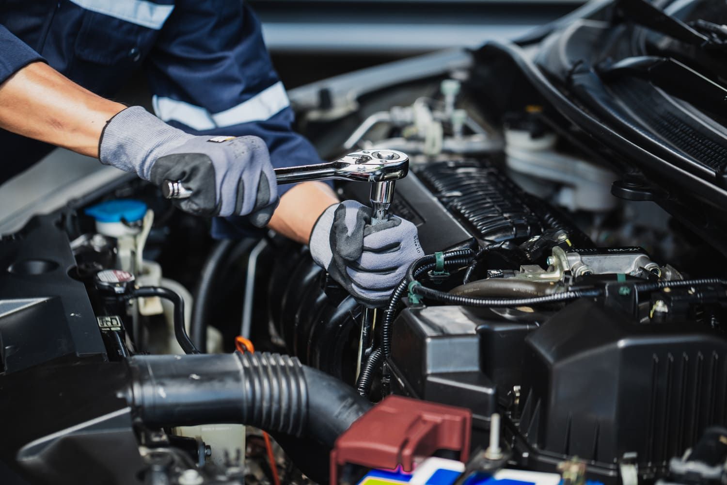 Technician tightening components in a car&rsquo;s engine bay with a ratchet